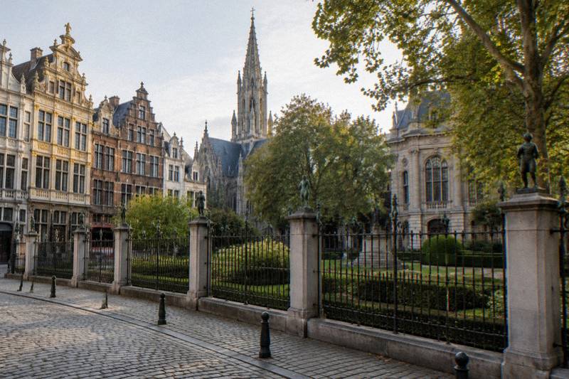 Mañana tranquila en la Square du Petit Sablon de Bruselas, Bélgica: un pequeño jardín formal con una verja de hierro forjado coronada por hileras de figuras de bronce sobre pilares de piedra, setos recortados, la aguja gótica de una iglesia sobre los árboles, sin nadie en la imagen.