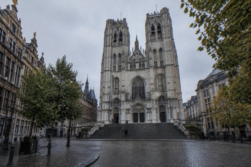 Cool overcast morning on the broad stone steps below the Cathedral of St Michael and St Gudula in Brussels, Belgium, the pale Gothic twin-towered front rising above, damp steps, a few tiny distant figures.