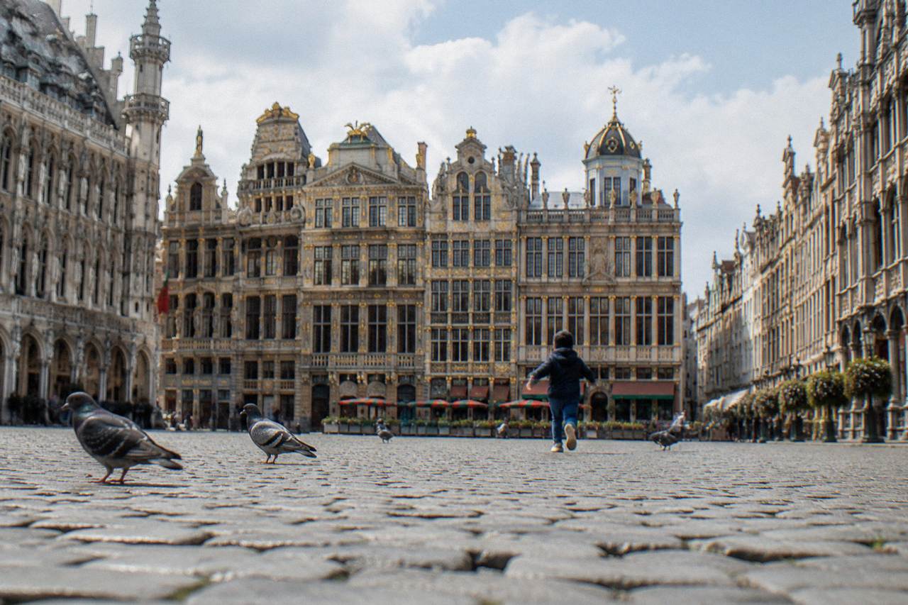 A wide stone square in Brussels with ornate gilded guild buildings under a daytime sky