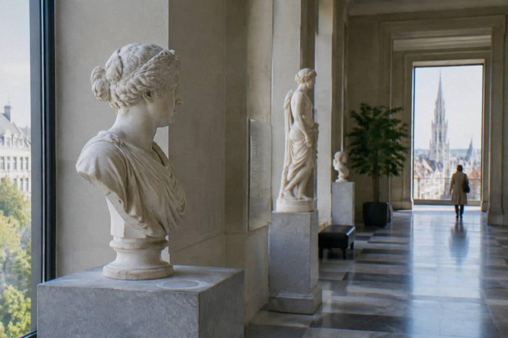 A museum interior in Brussels with classical sculptures displayed along a bright gallery corridor