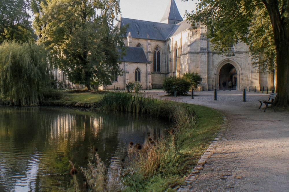 Stone abbey building with a courtyard entrance seen from a garden path
