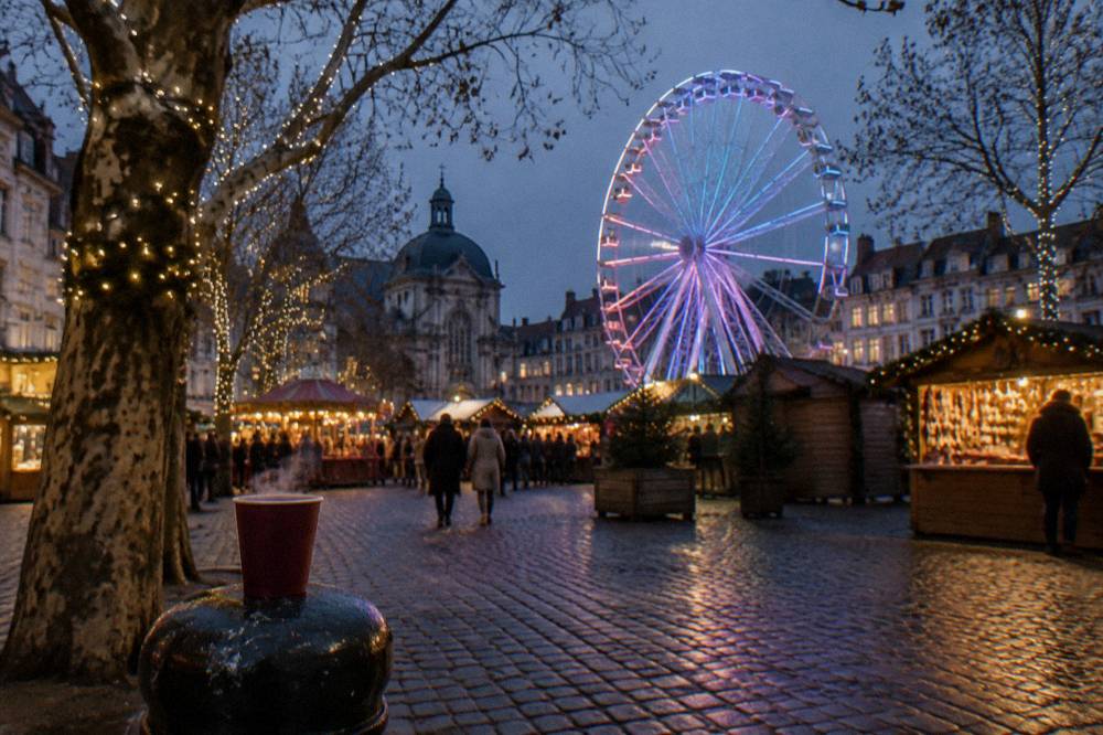 Illuminated market stalls and a ferris wheel against a dark evening sky in a city square