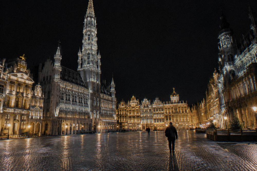 A floodlit gothic city hall tower above a decorated square at night