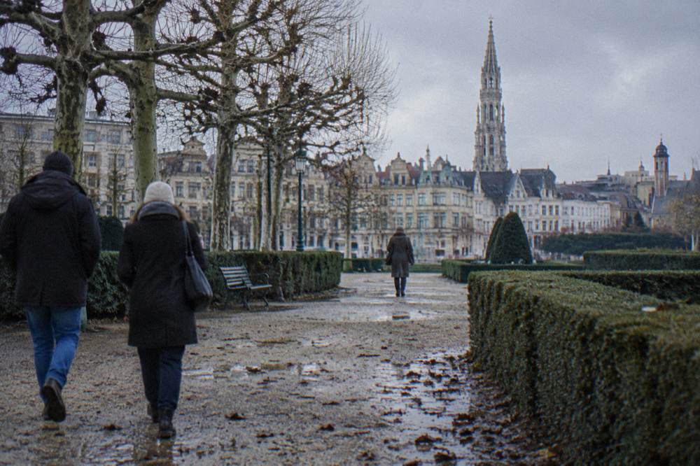 People in winter coats walking across a cobbled square with bare trees in Brussels