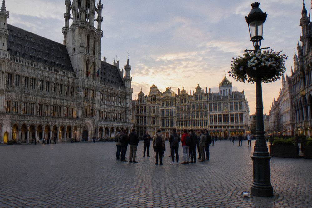 A group of visitors gathered around a guide near the Town Hall tower on the Grand-Place in Brussels