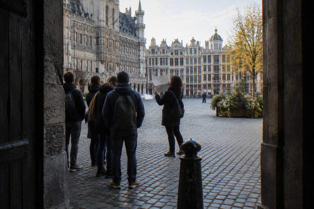 A guide holding up a folded map while speaking to walkers in a Brussels square
