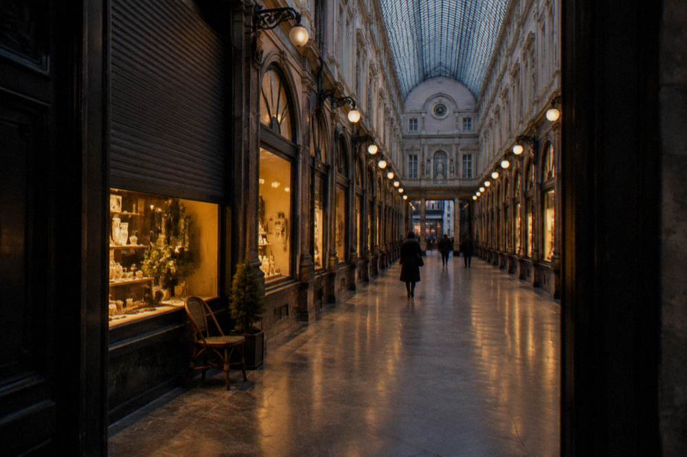 A covered arcade interior at dusk with warm light from shopfronts reflecting on the polished floor