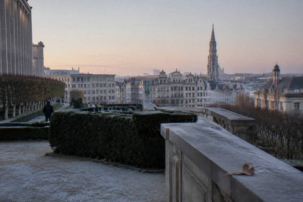 A formal public garden with trimmed hedges and a broad terrace overlooking a city skyline