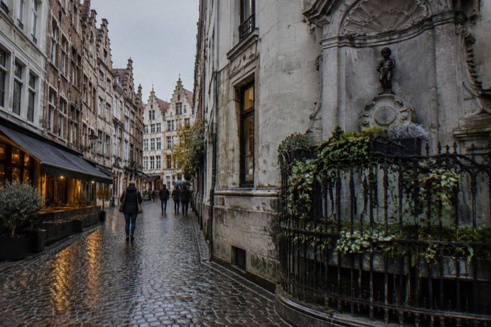 A narrow Brussels street corner with a small bronze fountain statue and stone facades