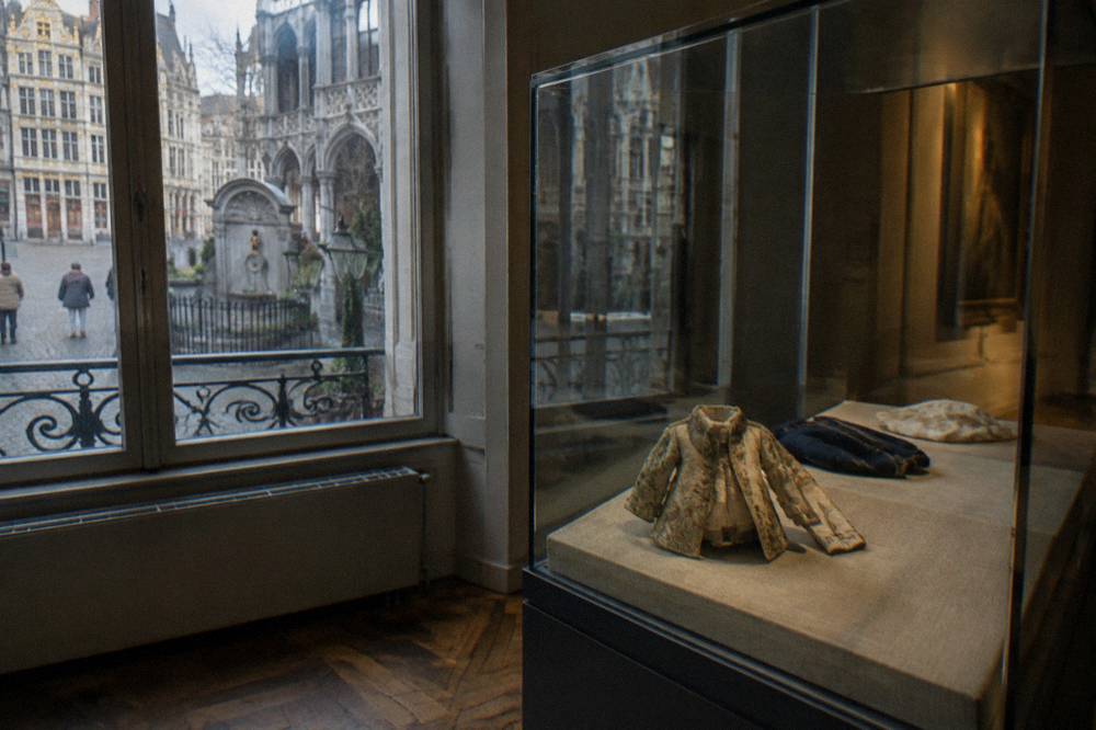 A museum display case with folded garments behind glass in a dim gallery