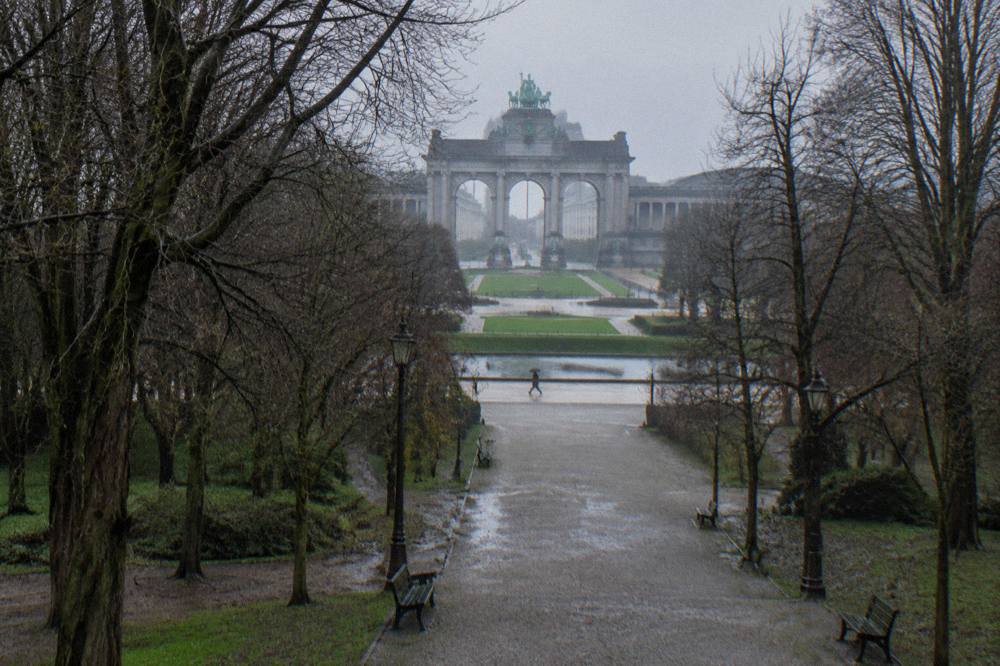 Tree-lined paths and open lawns in a large city park with a monumental arch in the background
